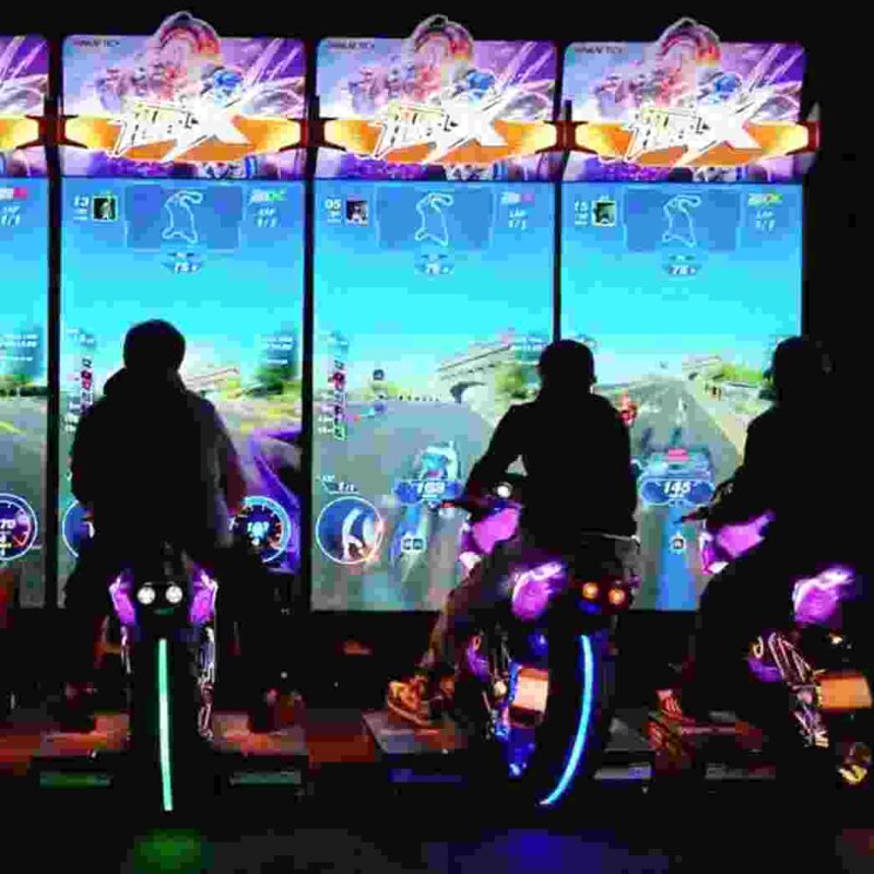 three players using motorcycle arcade machines